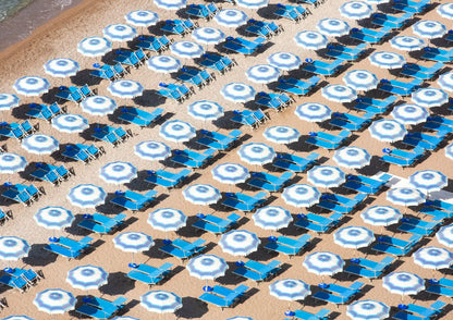 Pattern of blue and white umbrellas and lounge chairs on a sandy beach.