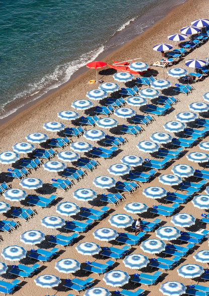 Beach scene with rows of blue and white umbrellas and lounge chairs on a sandy shore.