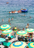 People enjoying the beach with colorful umbrellas and boats in the water.