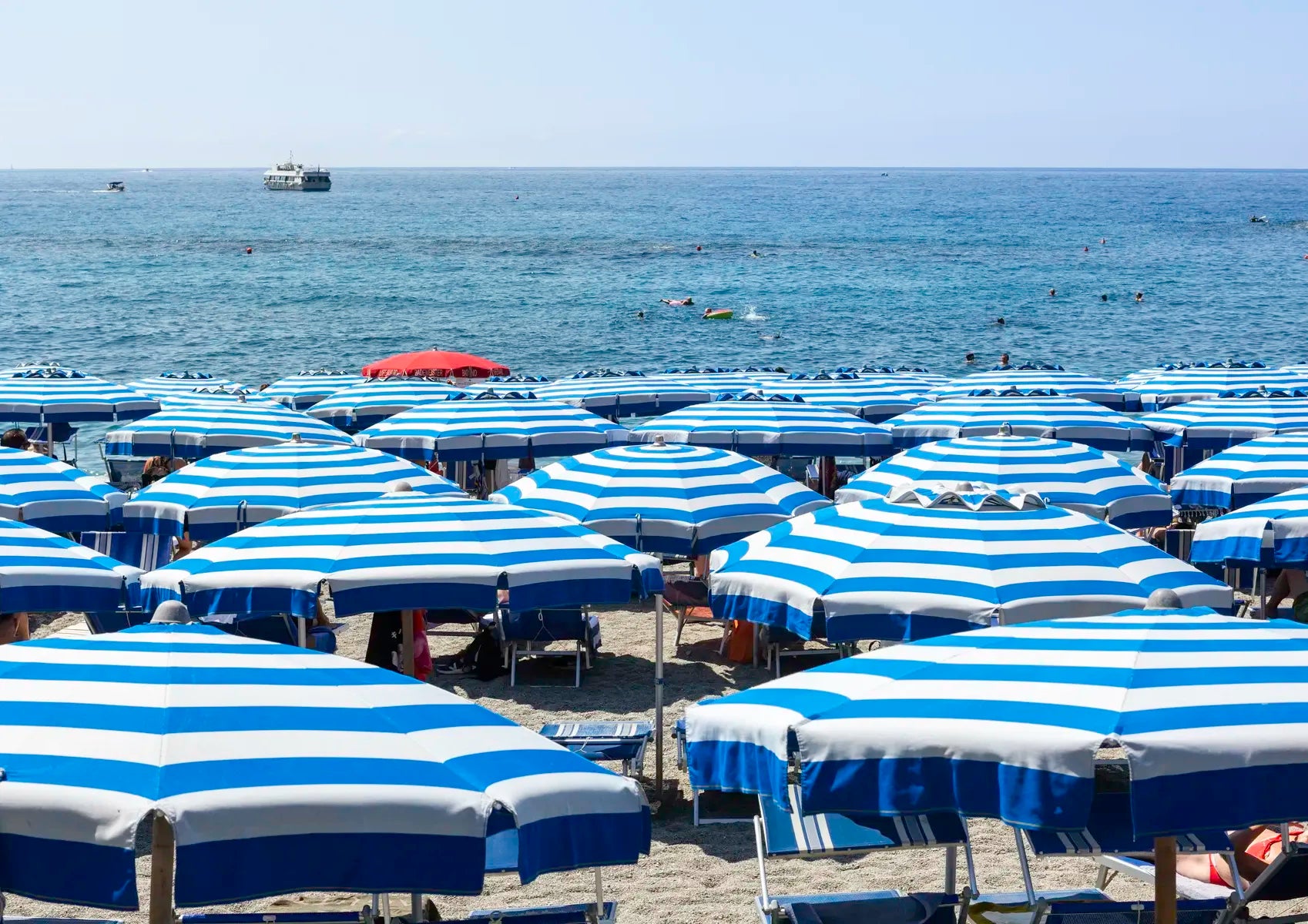 Beach scene with blue and white striped umbrellas and chairs on a sandy beach.
