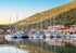 Marina with sailboats docked along a coastal hillside with buildings.