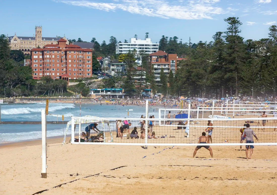Beach volleyball game on a sandy court with buildings and trees in the background