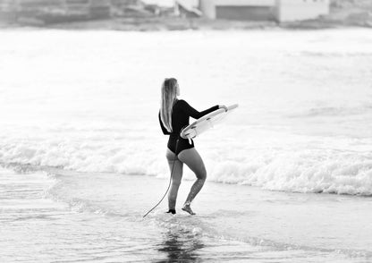 Person holding a surfboard walking into the water