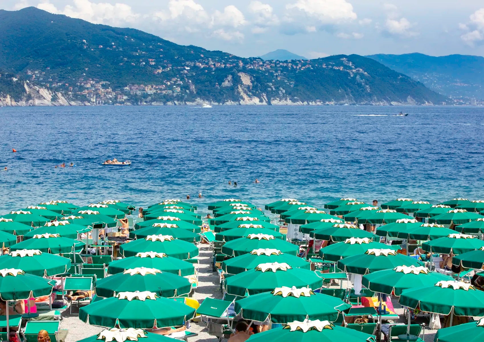 Umbrellas and people on a beach with mountains and ocean in the background