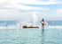 Person with a surfboard standing in a pool of water looking at the ocean.