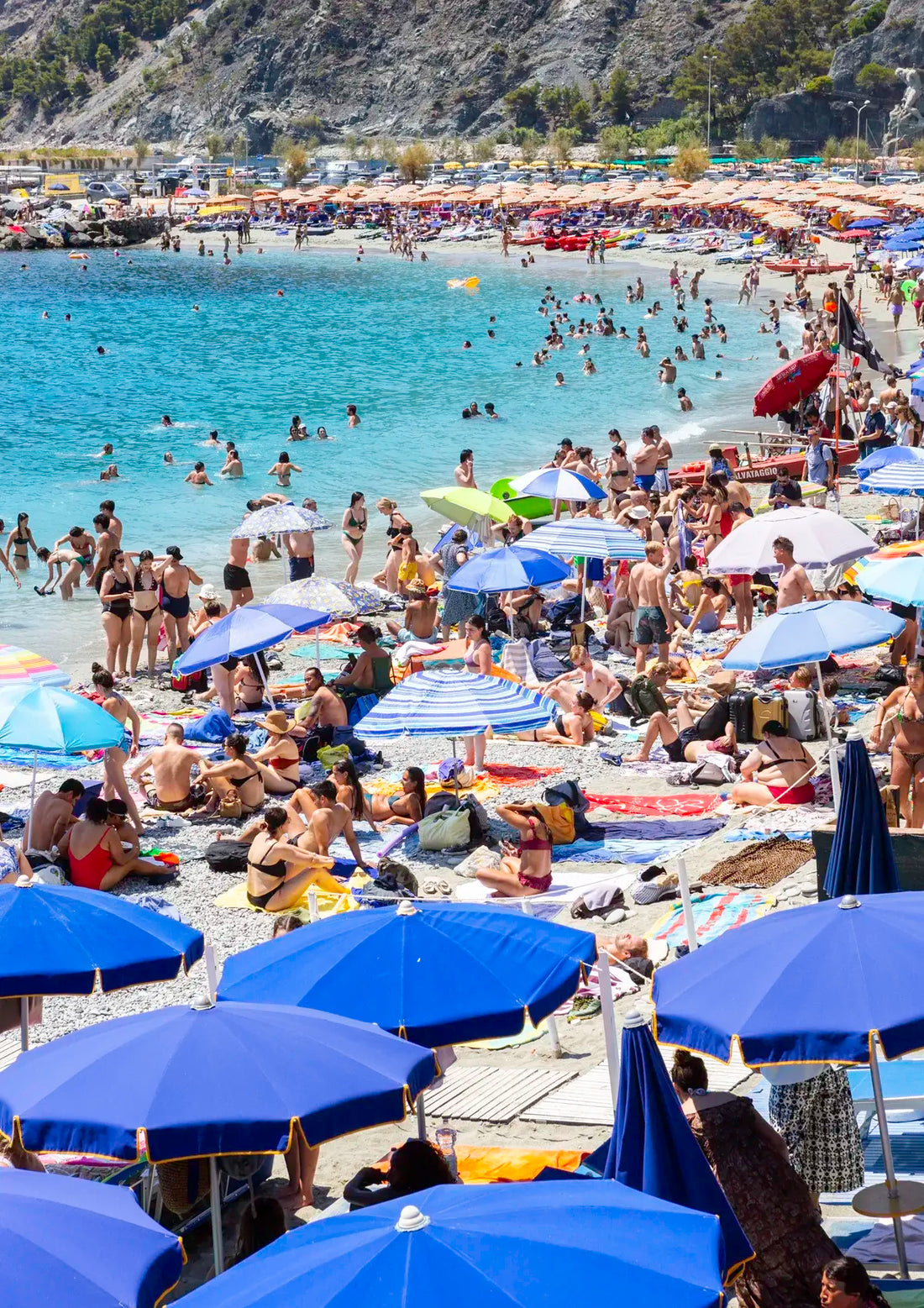  crowded beach with people, umbrellas, and mountains in the background