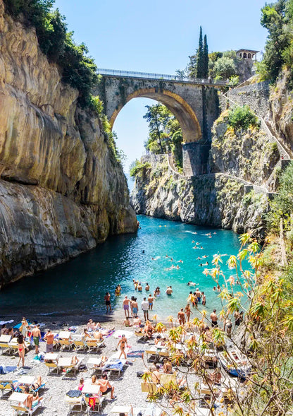 People enjoying a beach at a natural archway between two cliffs.