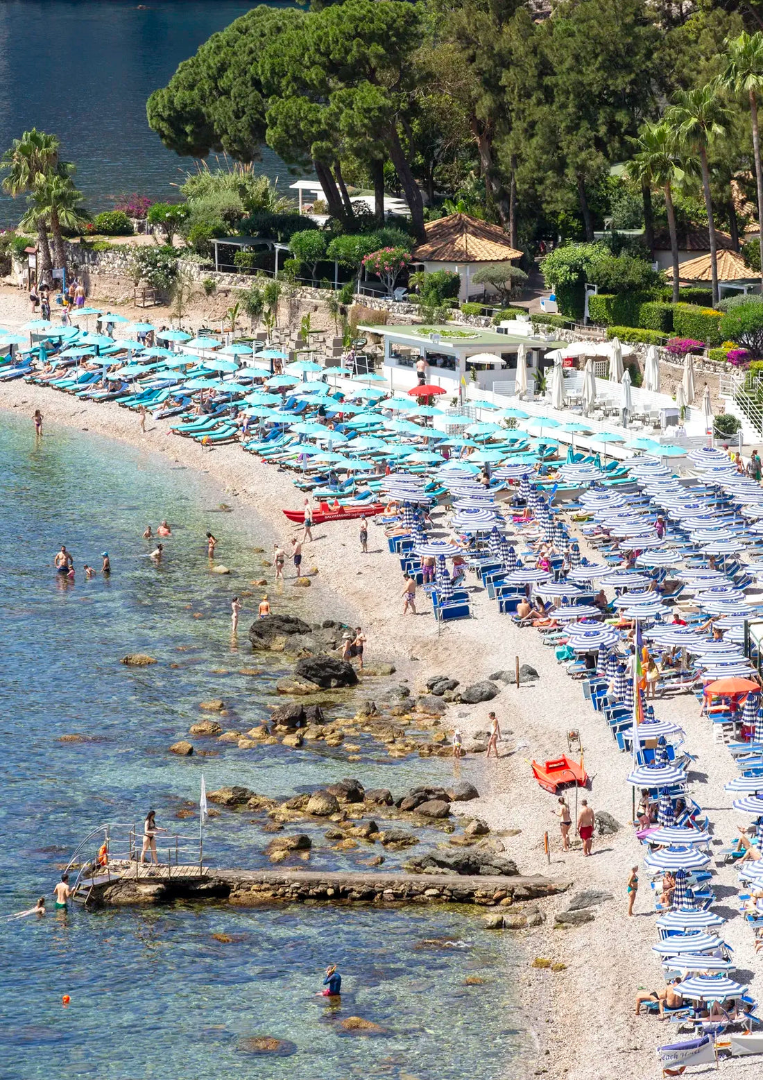 Beach scene with blue umbrellas, white lounge chairs, and people enjoying the water.