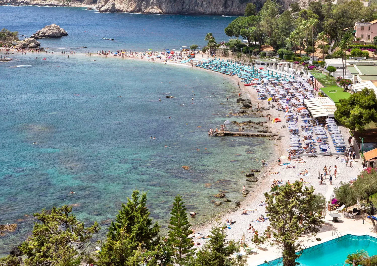 Beach scene with clear blue water, people, and a pool.