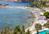 Beach scene with clear blue water, people, and a pool.
