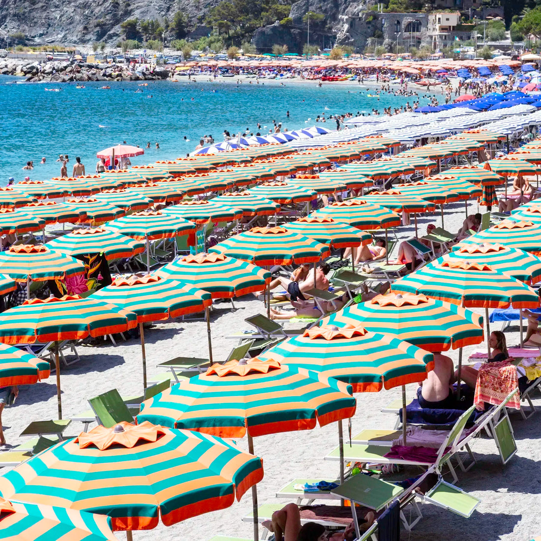 Beach scene with rows of striped umbrellas and people under them, near a body of water.