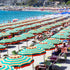 Beach scene with rows of striped umbrellas and people under them, near a body of water.