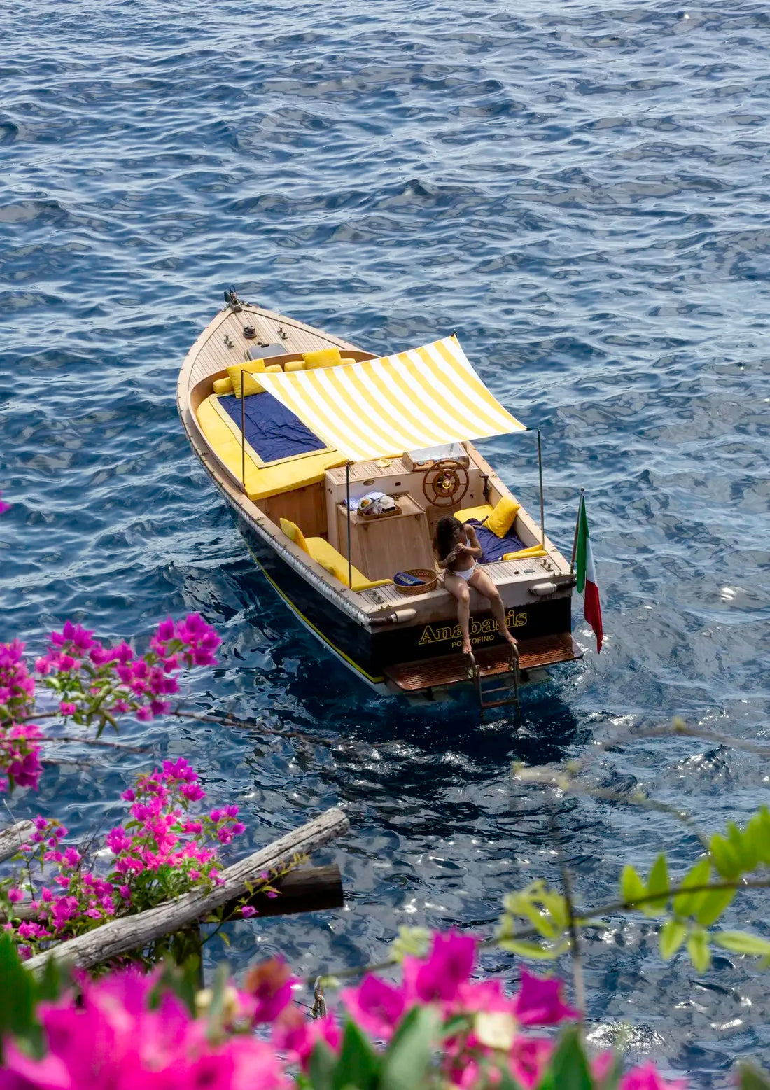 Small boat with a canopy on a body of water, surrounded by pink flowers and greenery.