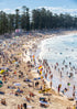 Crowded beach with people, umbrellas, and flags under a clear blue sky.
