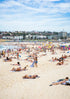 People sunbathing on a crowded beach with buildings in the background