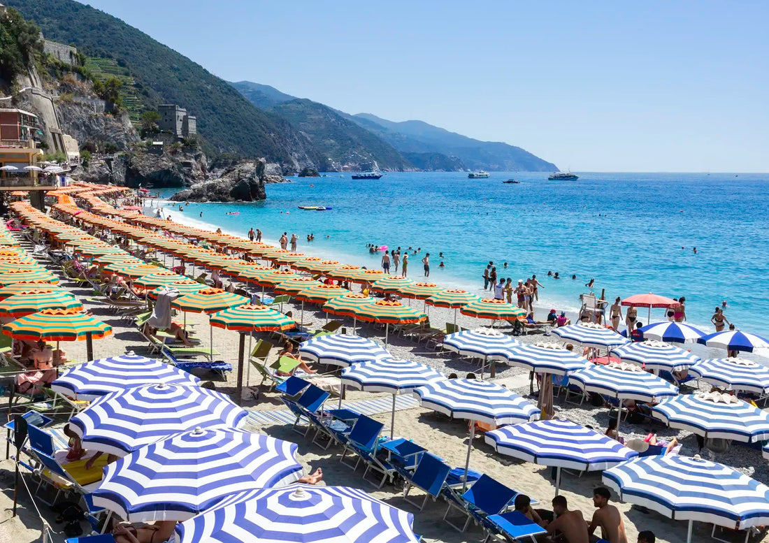 Beach scene with striped umbrellas, chairs, and people enjoying the sun by the ocean.