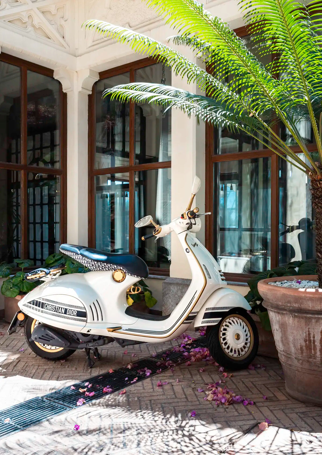White scooter parked in a decorative outdoor setting with plants and a building in the background.
