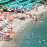 Beach scene with people sunbathing, swimming, and under umbrellas.