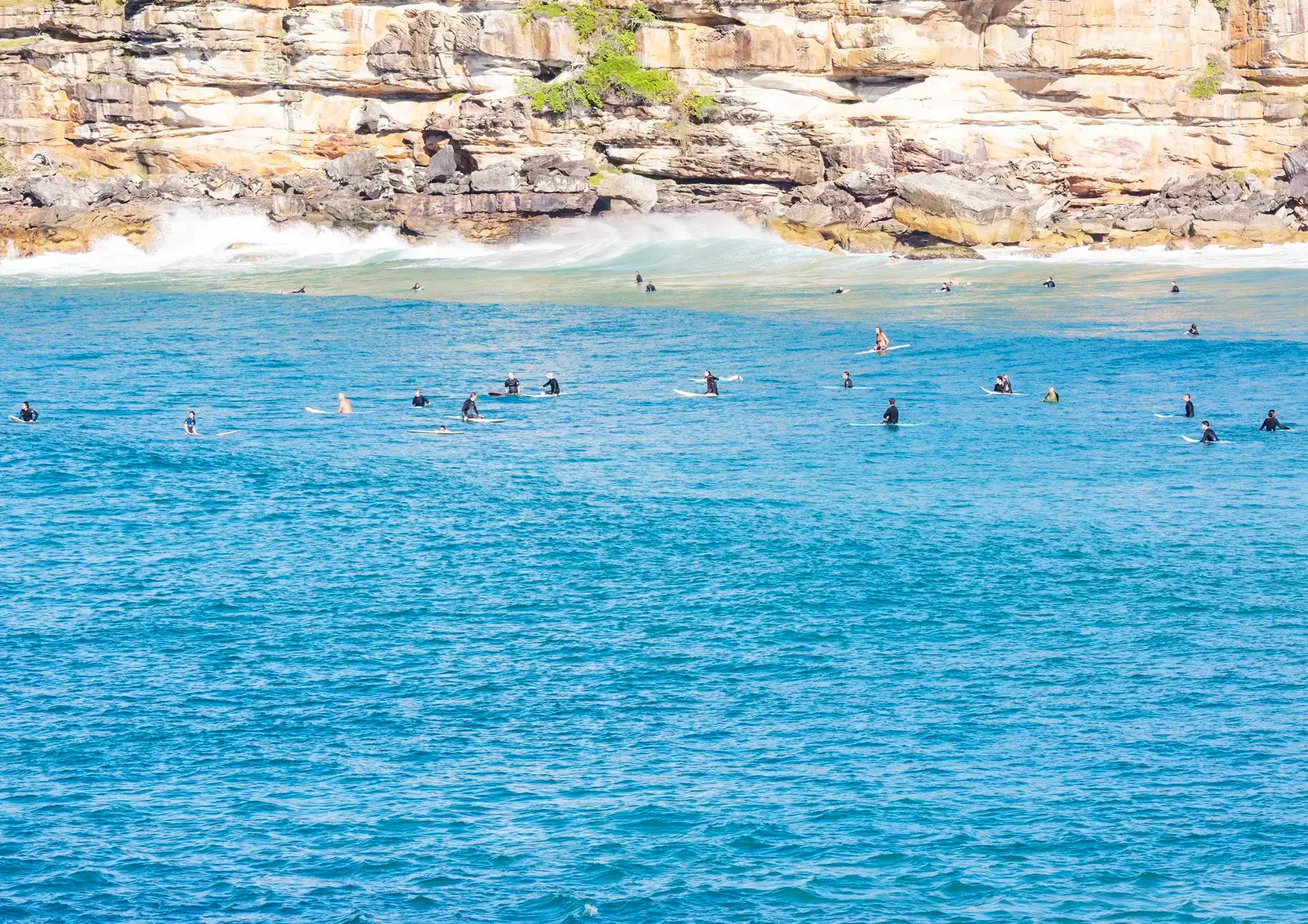 Surfers in the water with a rocky cliff in the background