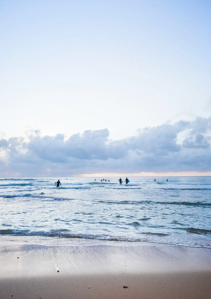 People surfing on a beach with a cloudy sky
