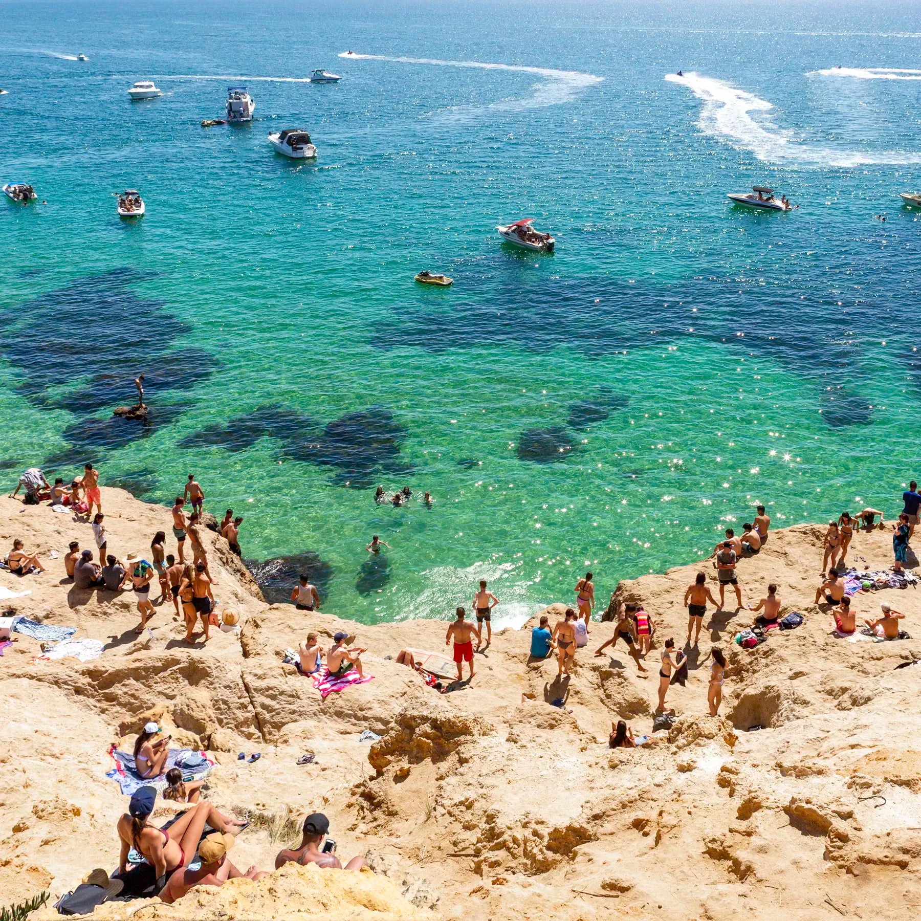 People enjoying a sunny day at a rocky beach called The Pillars in Mount Martha with clear blue water and boats in the background.