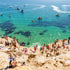 People enjoying a sunny day at a rocky beach called The Pillars in Mount Martha with clear blue water and boats in the background.
