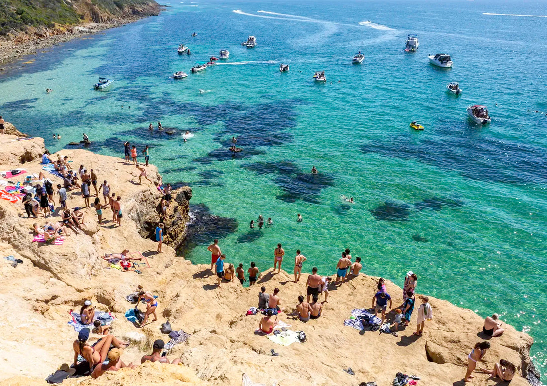People enjoying a sunny day at a rocky beach called The Pillars in Mount Martha with clear blue water and boats.