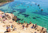 People enjoying a sunny day at a rocky beach called The Pillars in Mount Martha with clear blue water and boats.