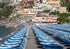 Beach with rows of blue umbrellas and chairs, buildings in the background.