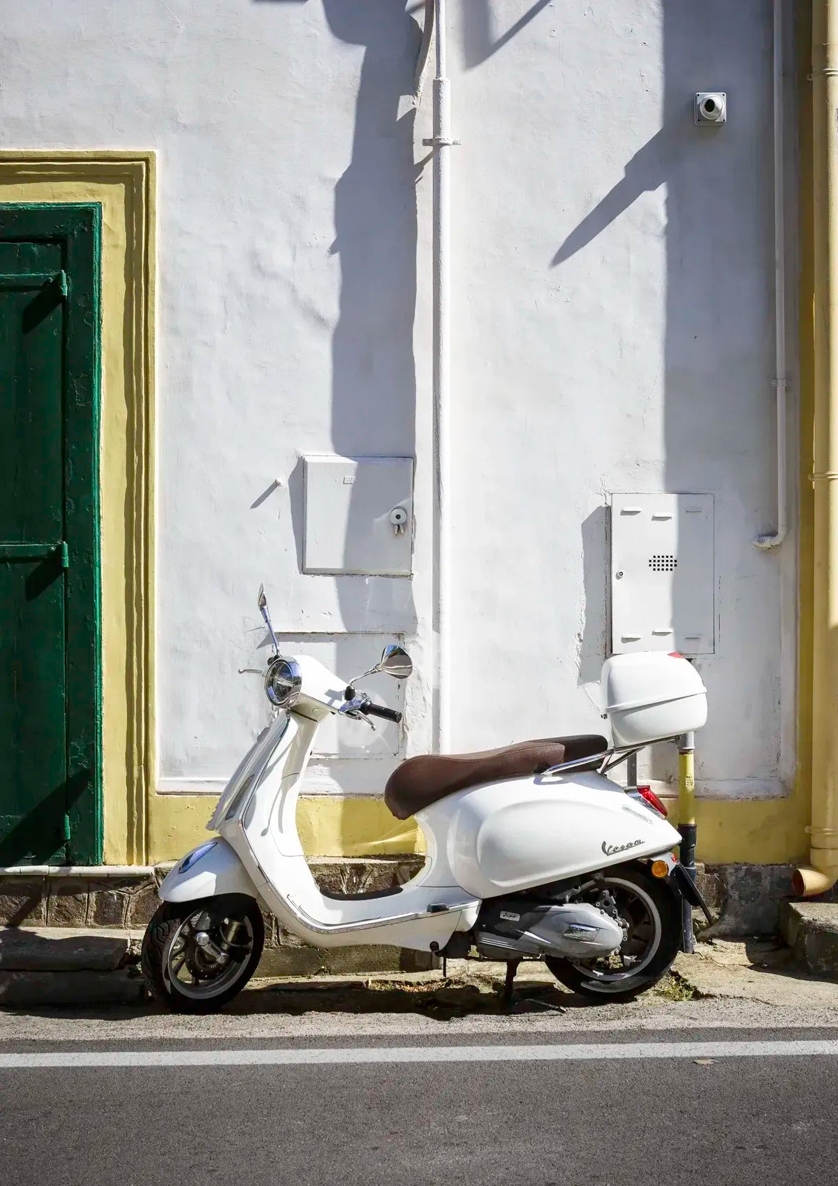 White scooter parked against a white wall with a green door.