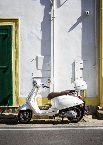 White scooter parked against a white wall with a green door.
