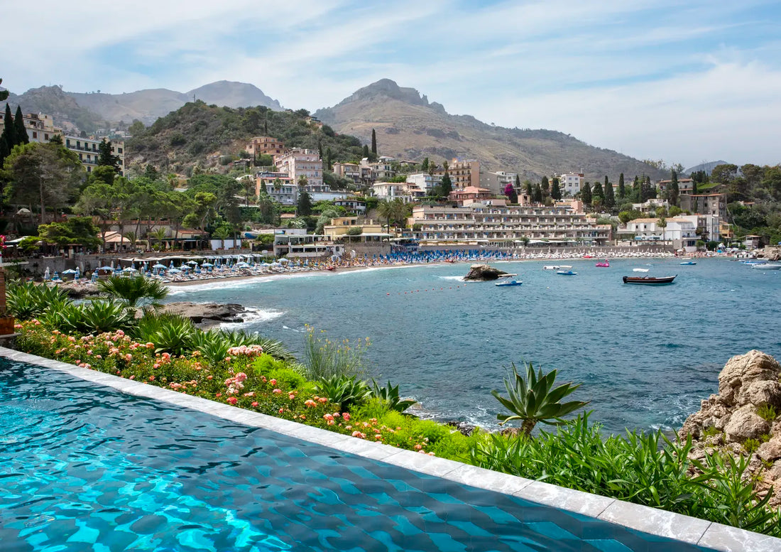 Hillside town with a beach and mountains, viewed from an infinity pool.