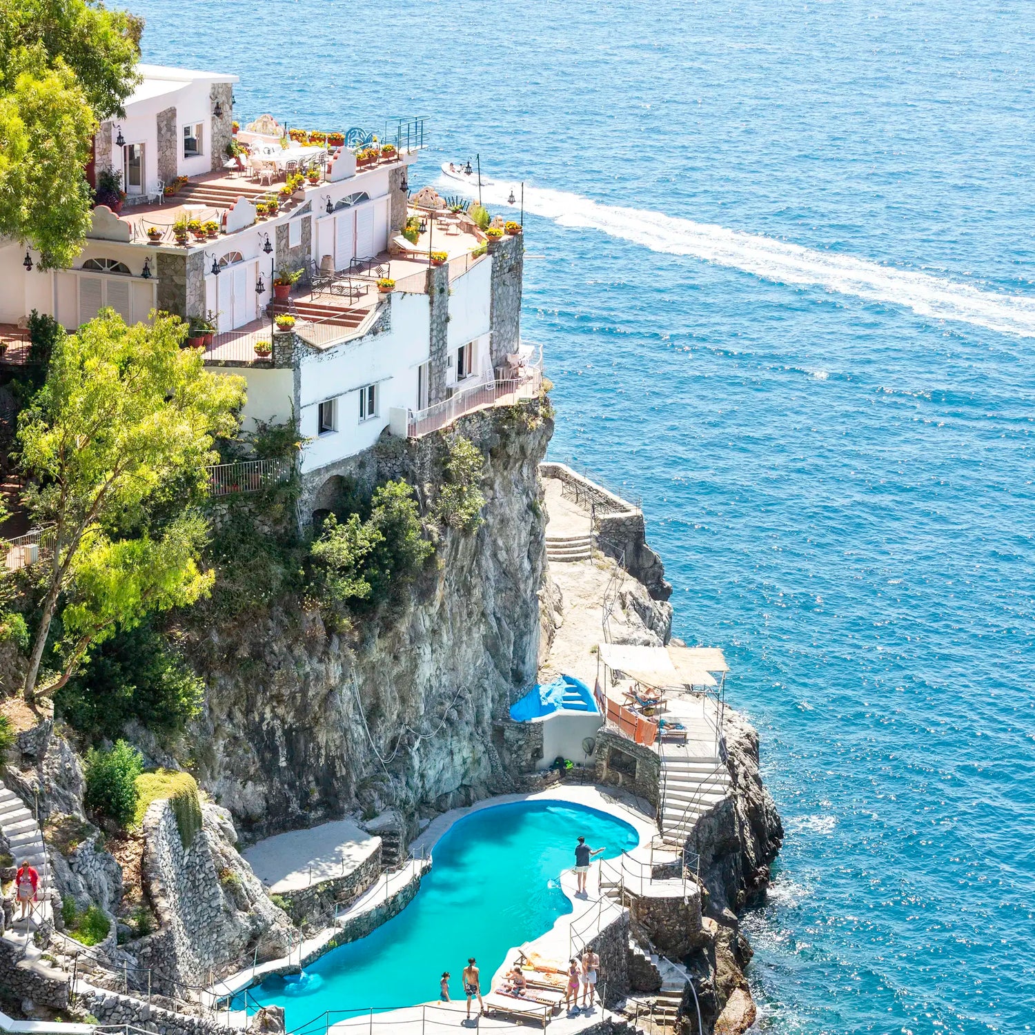 Crescent-shaped pool with white lounge chairs on a cliff overlooking the ocean.