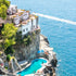 Crescent-shaped pool with white lounge chairs on a cliff overlooking the ocean.