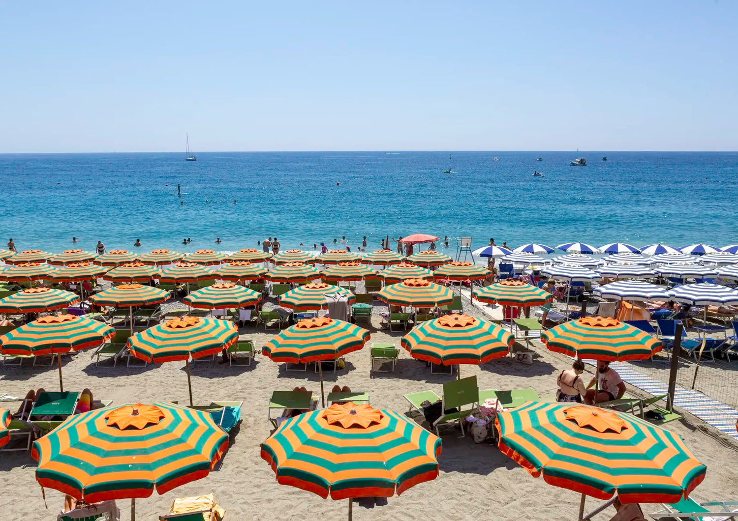 Beach scene with colorful umbrellas and lounge chairs under a clear blue sky.
