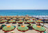 Beach scene with colorful umbrellas and lounge chairs under a clear blue sky.