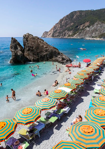Beach scene with colorful umbrellas, chairs, and people on a rocky coastline.