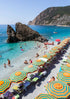 Beach scene with colorful umbrellas, chairs, and people on a rocky coastline.